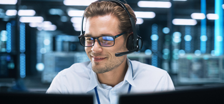 Person sitzt mit aufgesetztem Headset an einem Helpdesk