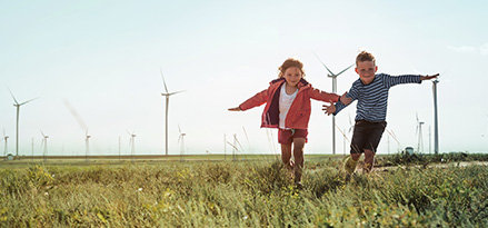 Zwei Kinder spielen auf einem Feld mit Windturbinen im Hintergrund